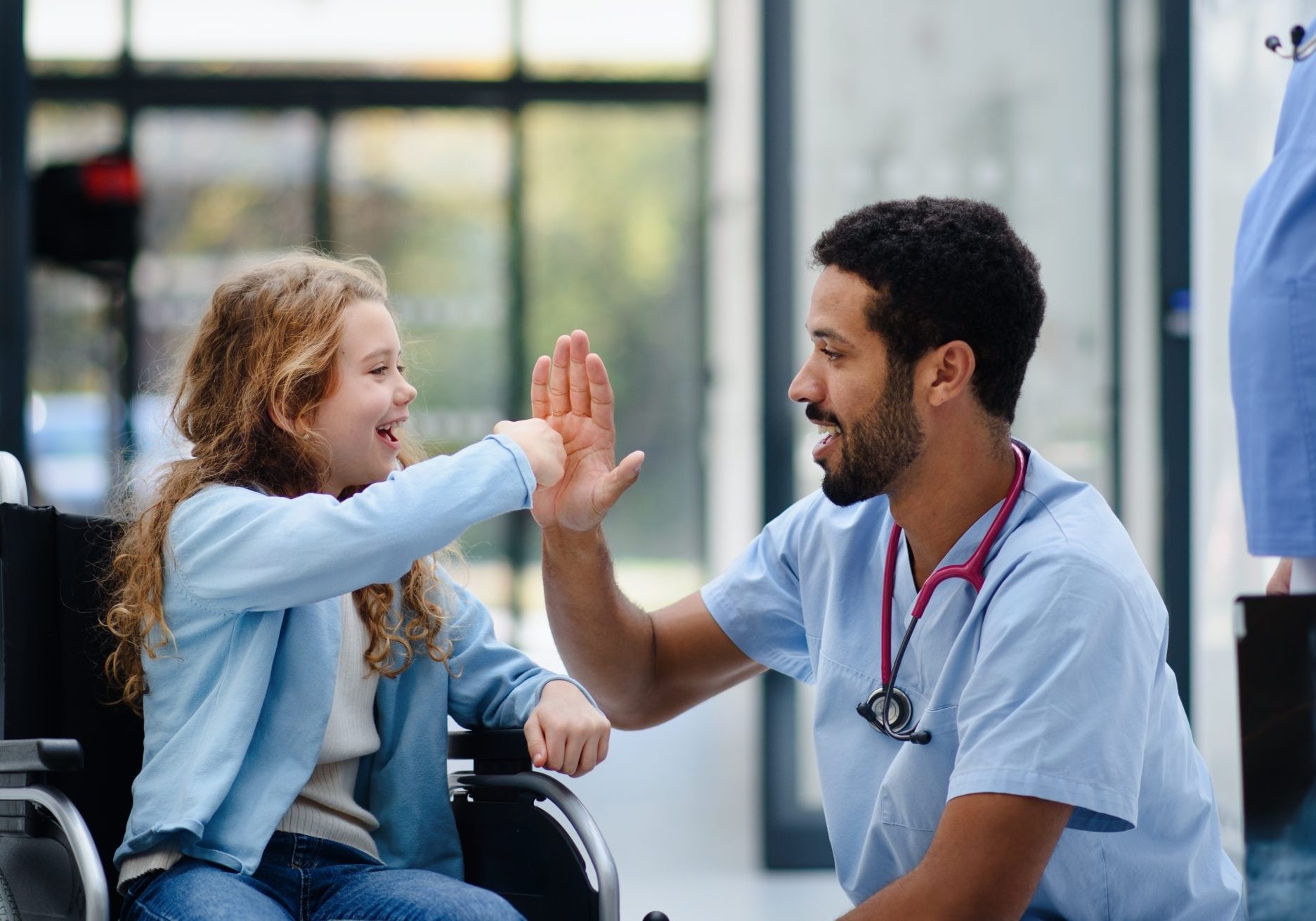 Young,Multiracial,Doctor,Having,Fun,With,Little,Girl,On,Wheelchair.